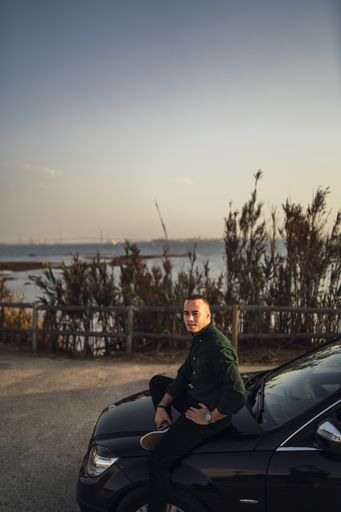 A vertical shot of a young man sitting on the car during daytime