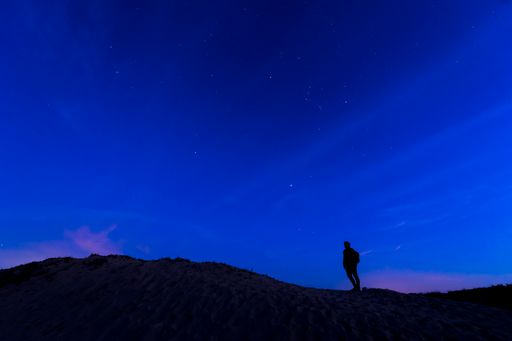 A low angle shot of a man standing in nature under a night sky with hills on the side