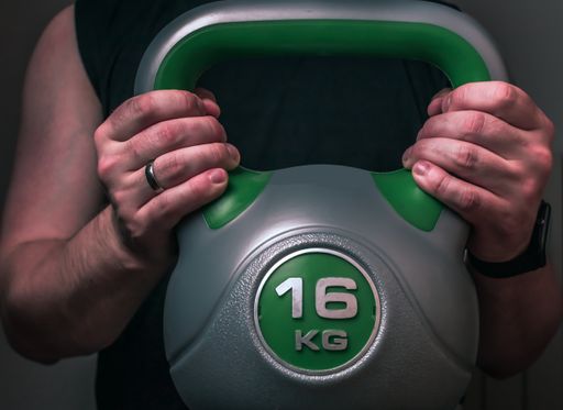 Kettlebell on a black background . The fist of an athlete grasping kettlebell . Close-up of a muscular hand holding a kettlebell.