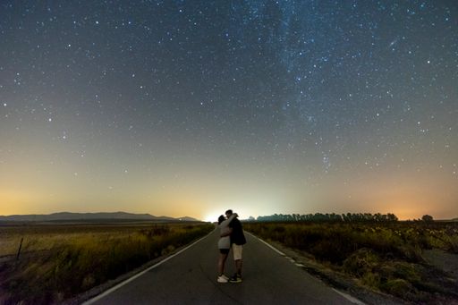 A couple hugging in the middle of the road under a starry  night sky