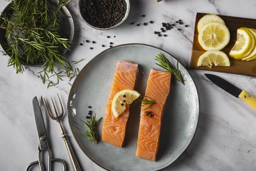 A top view of two salmon fillets with lemon, rosemary twig, and pepper on the table