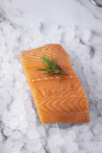 A vertical shot of salmon fillet with a sprig of rosemary on ice on a white marble background