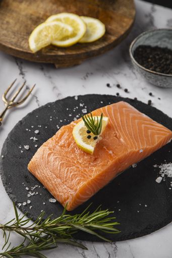 A vertical shot of raw salmon fillet with a lemon slice and rosemary on the table