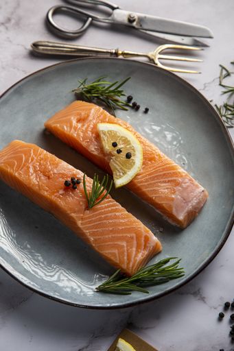 A vertical shot of two salmon fillets with lemon, rosemary twigs, and pepper