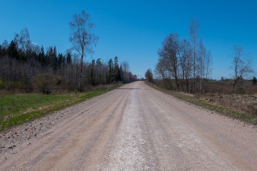 An empty dirt road through the countryside under a clear blue sky