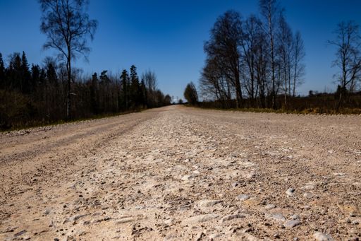 An empty gravel dirt road through the countryside under a clear blue sky