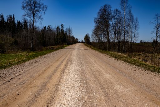 An empty gravel dirt road through the countryside under a clear blue sky