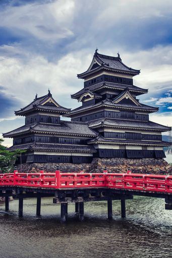 Photo of Matsumoto black castle in Nagano Prefecture, Japan. View from the side with the red bridge and the moat in the foreground.