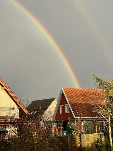 A vertical shot of a rainbow over houses in a village