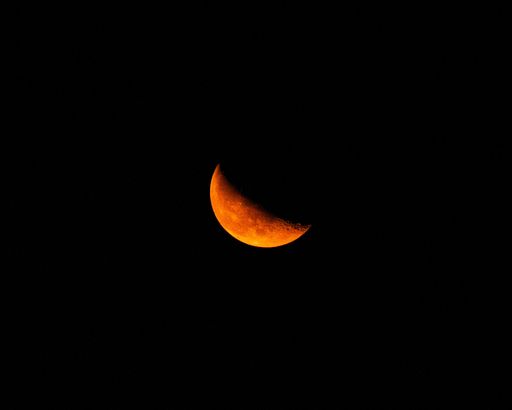 A picturesque view of a glowing orange crescent moon set against a night sky