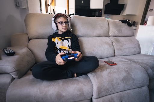A Spanish little boy playing an online videogame sitting on a sofa