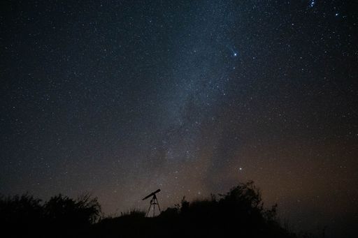 An astronomical telescope atop a hill, with the Milky Way galaxy illuminated in the background