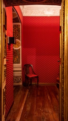 A vertical picture of a red chair in a hallway with red walls under the lights