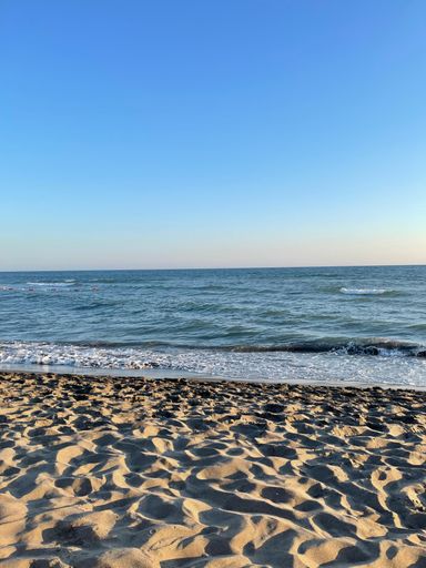 A stunning view of a sandy beach with crashing waves and a beautiful blue sky