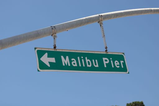 A green and white street sign pointing to Malibu Pier in California