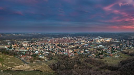 A landscape of hills covered in greenery surrounded by a town under a cloudy sky during the sunset