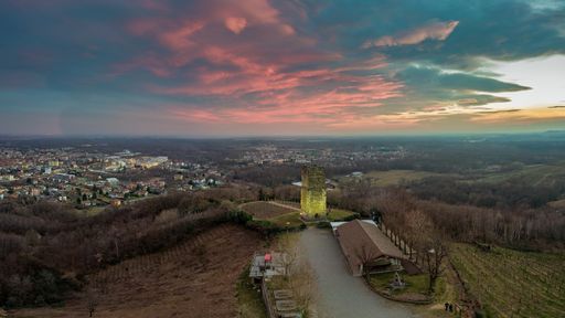 A landscape of hills covered in greenery surrounded by a town under a cloudy sky during the sunset