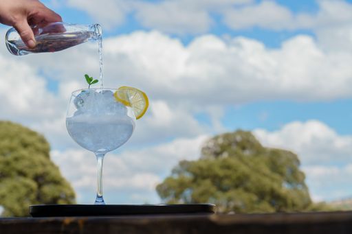 A woman's hand pouring tonic from a bottle into a glass with ice