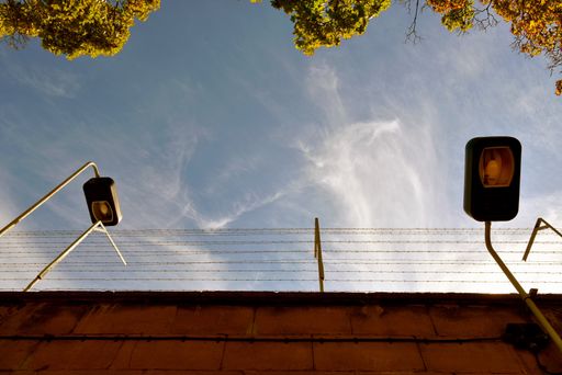 A low angle shot of a prison wall covered with barbed wires under the sunlight