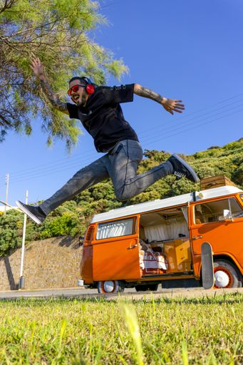 A man jumping iun the park with an orange Volswagen T2 camper