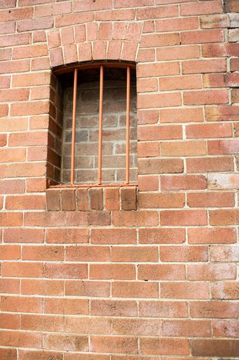 A vertical shot of a small window with lattices on a cobblestone wall