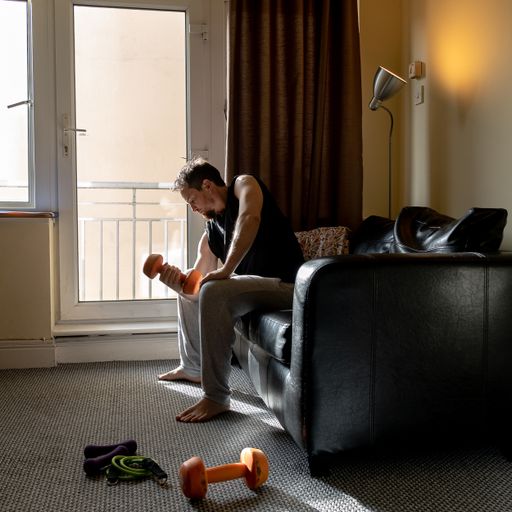 A young Caucasian man doing weight lifting at home sitting on a sofa