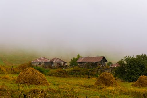 An idyllic rural scene featuring two large hay bales in a foggy meadow