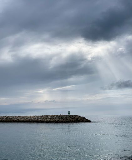 An aerial view of a lighthouse situated on a rocky seashore on a cloudy day