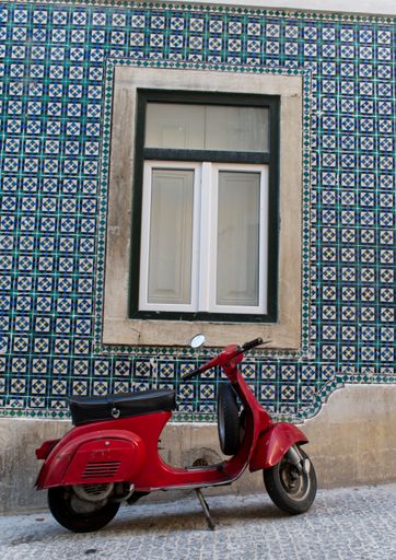 A vertical shot of a window with a red vintage scooter parked in the building
