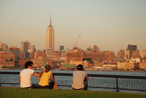 Young couple sitting on Hudson River waterfront enjoying the evening view to Manhattan skyline, New York Ci