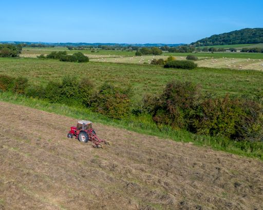 An aerial view of a tractor plowing a field of soil.