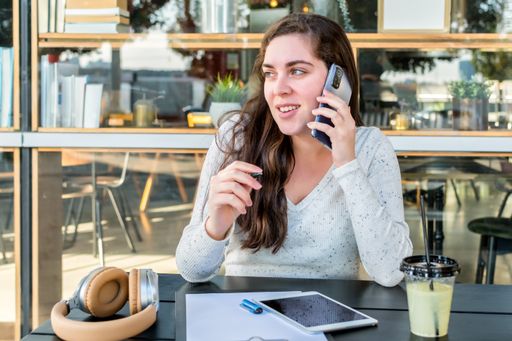 A young woman having a call via her smartphone while sitting in a street cafe