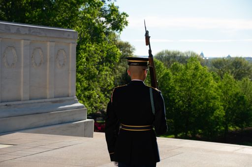 A soldier standing at attention and holding a rifle while in a uniform outside of a building