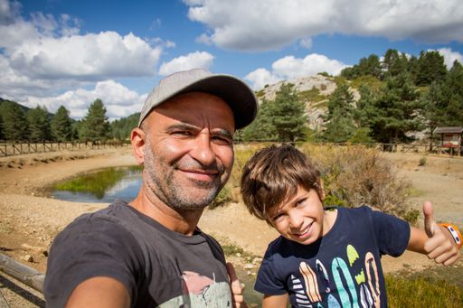 A happy Spanish father and son taking a selfie in a park under a bright sunlight