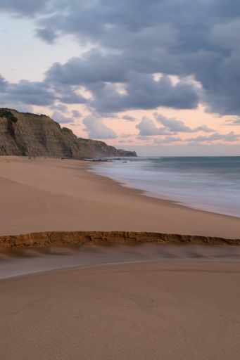 A vertical shot of sandy beach and wavy sea at sunset