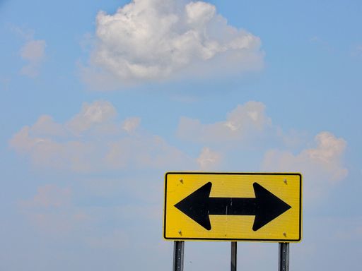 An isolated yellow and black double arrow road sign with a cloudy blue sky in the background