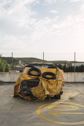A vertical shot of an abandoned pickup truck covered with a yellow tarpaulin at a car park
