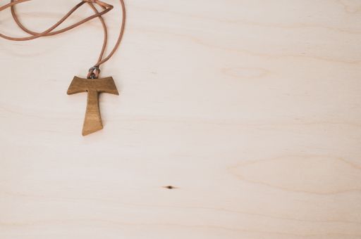 A top view of a wooden tau cross necklace on a wooden surface for a copy space