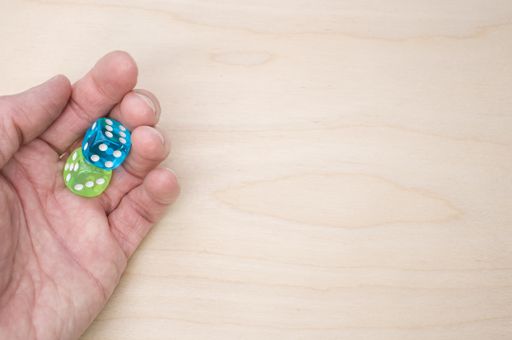 A top view of a hand holding green and blue dice isolated on a wooden surface for a copy space