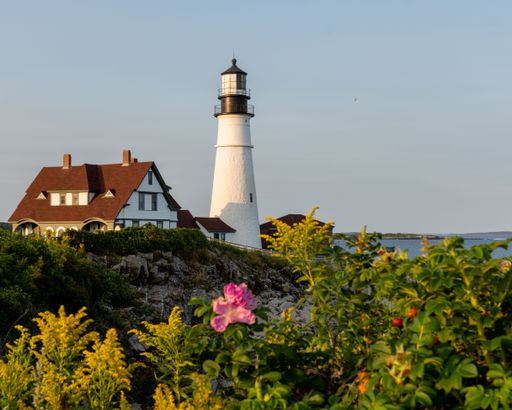 A majestic white lighthouse stands tall on a rocky cliff, overlooking a vast expanse of sparkling blue sea