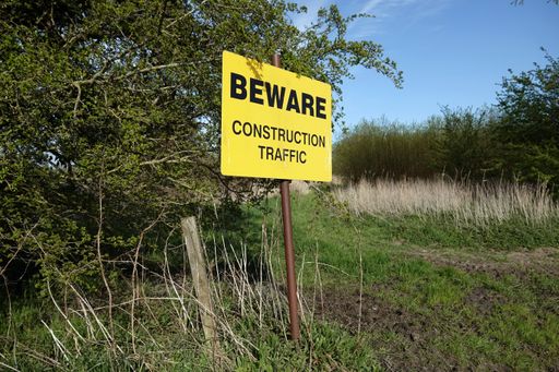 A yellow sign in the wild next to a tree warning about construction traffic