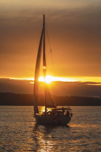A vertical shot of a sailing boat in the ocean during sunset