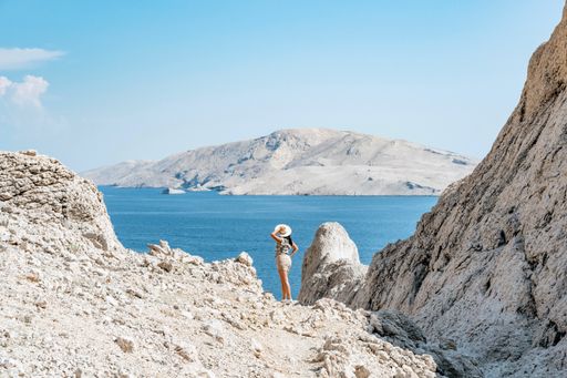 Tiny human in big world. Young tourist standing on ridge overlooking amazing coastline and sea on Pag island in Croatia.