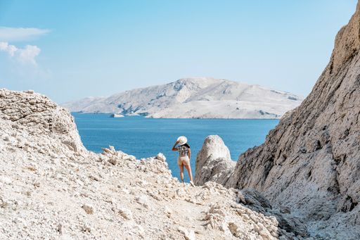 Tiny human in big world. Young tourist standing on ridge overlooking amazing coastline and sea on Pag island in Croatia.