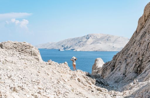 Tiny human in big world. Young tourist standing on ridge overlooking amazing coastline and sea on Pag island in Croatia.