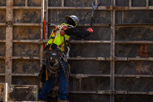 A construction worker wearing a yellow vest is performing construction work on a building
