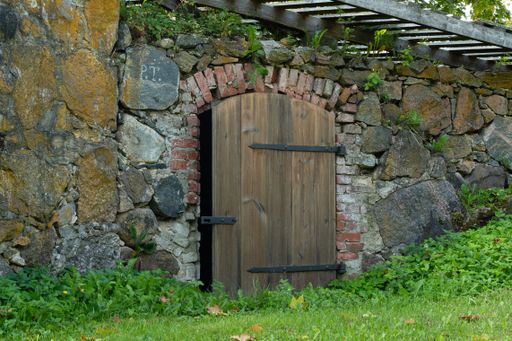A wooden door with an intricate brick and iron gate on an old stone building