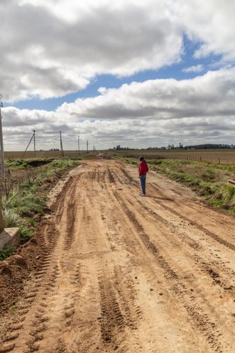 A man standing alone on a rural muddy road through farmlands under a cloudy sky