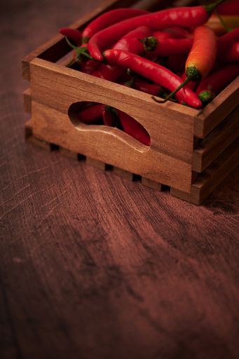 Several red chili peppers in a box put on a wooden surface