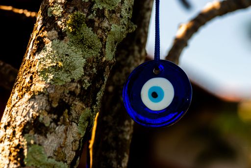 A purple evil eye charm hangs from a tree branch against the backdrop of a warm, golden sunset